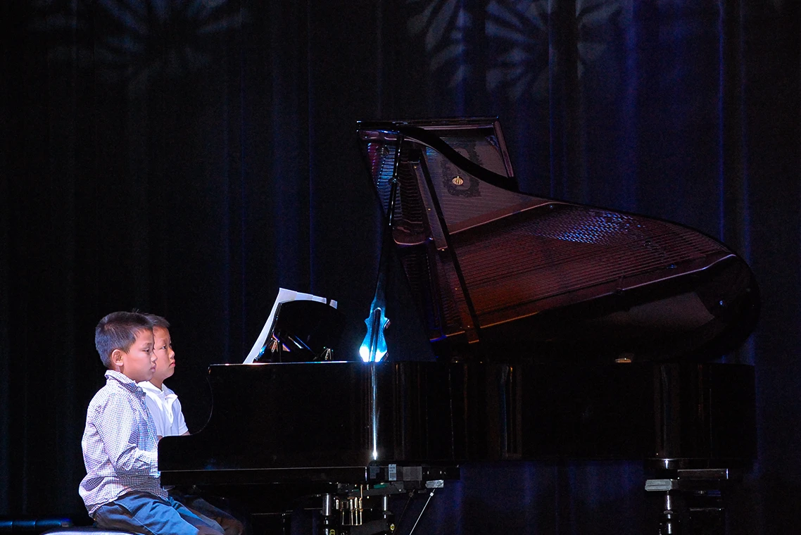 beginner piano students play a duet on a grand piano